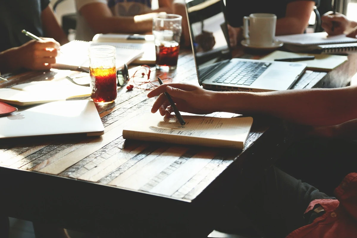 Table de travail : plusieurs personnes rédigent et relisent des textes autour d’ordinateurs portables